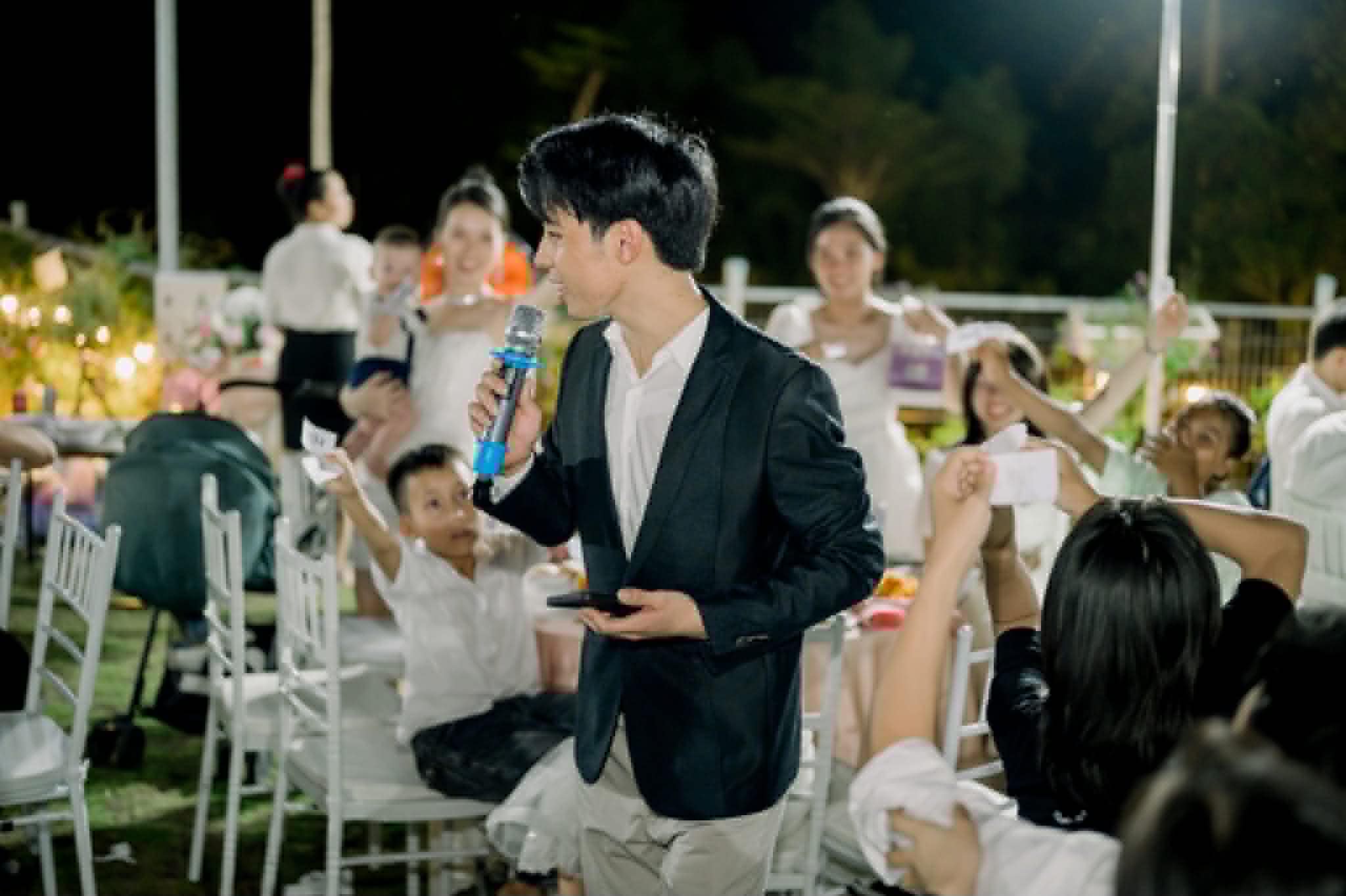Thanh Hiếu cầm mic đi giữa bàn tiệc, khách giơ tay tham gia trò chơi